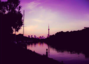 Toronto skyline and CN Tower seen from Toronto Islands with purple sky.